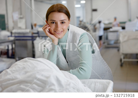 A woman smiles joyfully in a laundromat, surrounded by linens 132715918