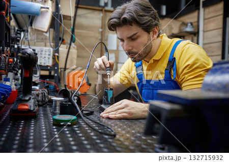 Skilled man worker is working on soldering iron in a workshop Skilled man worker is working on soldering iron in a workshop 132715932