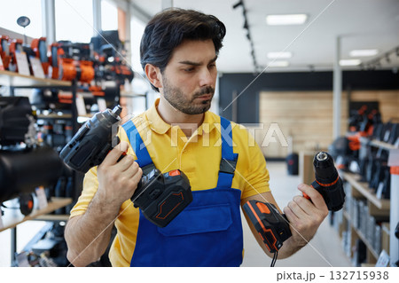 A man worker is holding impact and power drills in his hands in a store 132715938