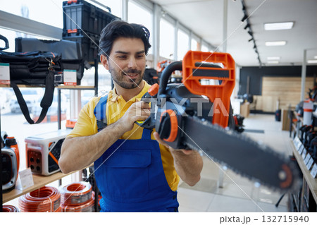 Worker is standing in a store holding a chainsaw tool 132715940