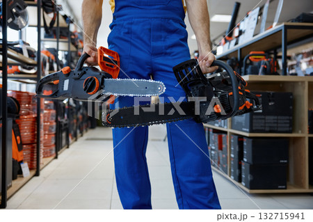 A man worker holding two chainsaws inside a store 132715941