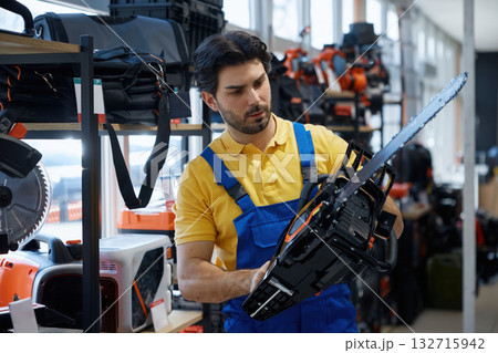 A man worker is holding a chainsaw inside a hardware store 132715942