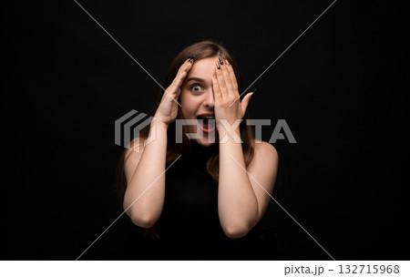Surprised young woman with long brown hair covering mouth with hand on blue background Surprised young woman with long brown hair covering mouth with hand on blue background 132715968