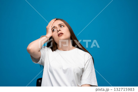 Tired young woman with long brown hair touching forehead and rolling eyes on blue background 132715983