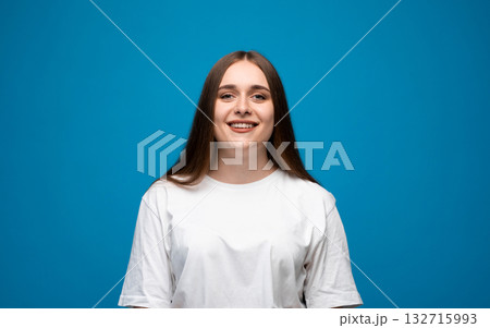 Smiling young woman with long brown hair and blue eyes wearing white t-shirt on blue background Smiling young woman with long brown hair and blue eyes wearing white t-shirt on blue background 132715993