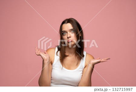 Confused young woman shrugging shoulders with questioning look on pink background 132715997