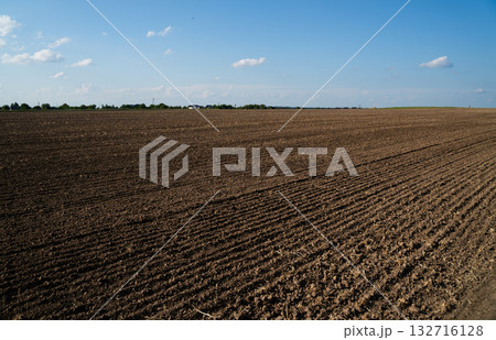 Freshly plowed brown soil field under clear blue sky in rural farmland landscape 132716128