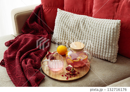 Glass Teapot and Teacup with Pomegranate Drink with Ginger and Citrus on Cozy Sofa with Autumn Decor 132716176