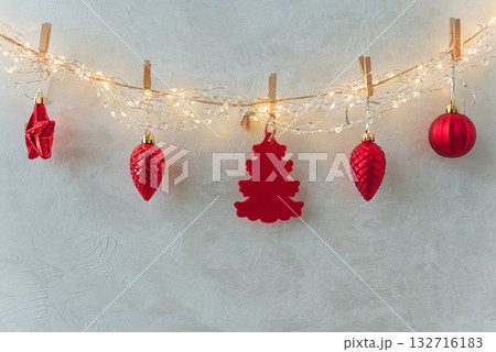 Red Christmas Ornaments Hanging on String Lights Against Textured Wall 132716183