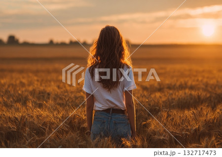 Woman Enjoys Sunset View Over Golden Wheat Field in a Serene Rural Setting 132717473