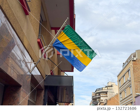 Flag of Gabon on a city building. Expression of national identity, architecture, and culture in an urban environment under soft daylight. 132721686