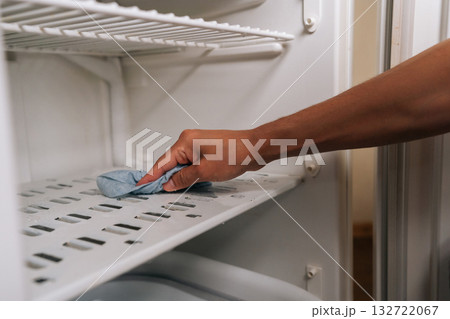 Person defrosting and cleaning interior of refrigerator using blue rag to wipe away ice and grime buildup, ensuring fresh and sanitary food storage environment. Concept of hygiene and cleanliness. Person defrosting and cleaning interior of refrigerator using blue rag to wipe away ice and grime buildup, ensuring fresh and sanitary food storage environment. Concept of hygiene and cleanliness. 132722067
