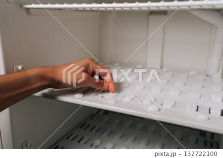 Fingertips pressing against thick frost layer inside refrigerator freezer, revealing heavy ice accumulation requiring urgent defrosting. Concept of need for defrosting due to excessive buildup. Fingertips pressing against thick frost layer inside refrigerator freezer, revealing heavy ice accumulation requiring urgent defrosting. Concept of need for defrosting due to excessive buildup. 132722100