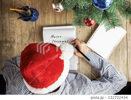 A guy in a Santa hat writes Merry Christmas on a white piece of paper 132722434
