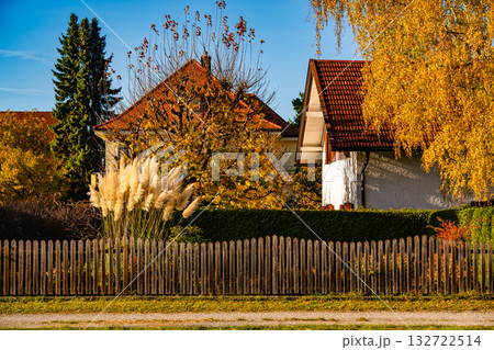 Charming Country House In Gilching, Bavaria: Cozy Home With Wooden Fence, Autumn Trees, And Warm Golden Light In Peaceful Village Setting 132722514