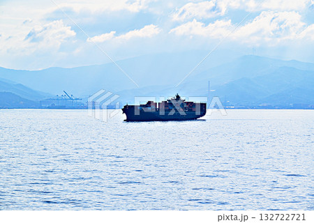 Silhouette of a cargo ship at sea against a blue sky on the horizon. 132722721