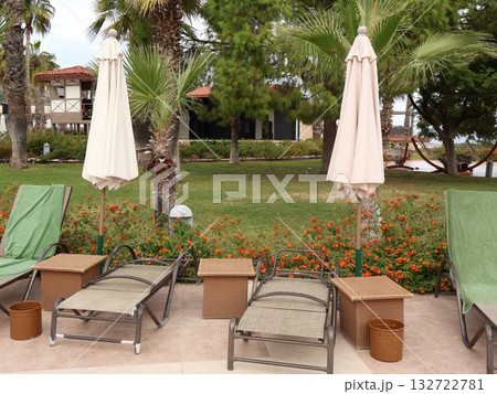 Relaxing Poolside Lounge Area With Umbrellas, Palm Trees, And Floral Garden At Resort 132722781
