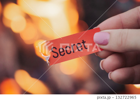 Female hand holding small red burning sheet of paper with word "secret" on it , close up. Concept of opening the truth, being sincere and honest Female hand holding small red burning sheet of paper with word "secret" on it , close up. Concept of opening the truth, being sincere and honest 132722965