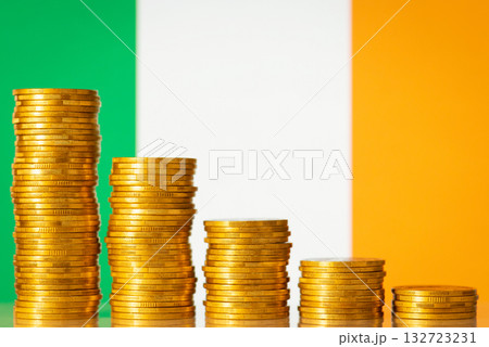 Five stacks of gold coins in front of flag of Ireland symbolizing crisis in economy of the republic. Regression of the economy 132723231