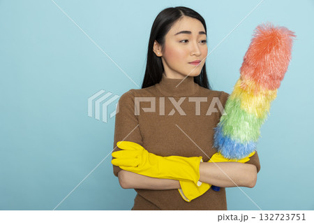 Pretty female janitor wearing yellow rubber gloves and standing with feather duster, prepared for cleaning services. Portrait of asian housekeeper posing with arms crossed, confident in completing 132723751