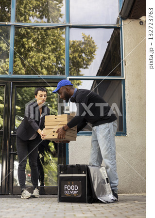 African american man delivering pizza in a large stack of cardboard boxes to a client standing in her doorway. The transaction is part of a routine, fast paced city courier service. African american man delivering pizza in a large stack of cardboard boxes to a client standing in her doorway. The transaction is part of a routine, fast paced city courier service. 132723763
