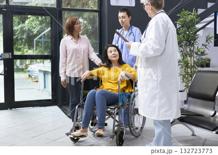 Medical staff assisting disabled asian woman to navigate hospital lobby during routine checkup. Focusing the conversation on accessibility needs and adjustments for independency. Medical staff assisting disabled asian woman to navigate hospital lobby during routine checkup. Focusing the conversation on accessibility needs and adjustments for independency. 132723773