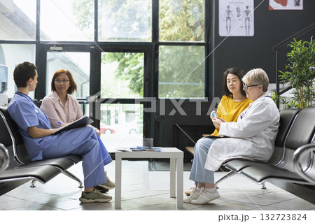 General practitioner preparing glucose test strip for sugar level monitoring in waiting room facility. Asian patient receives guidance on hyperglycemia warning signs and glucose control methods. 132723824