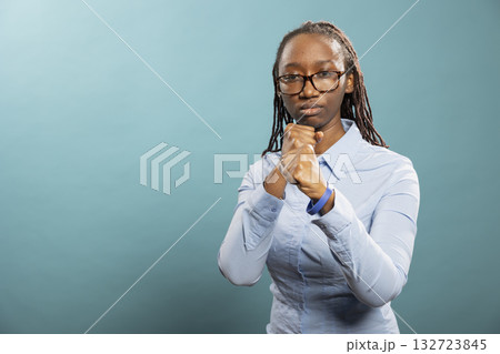 African american woman stands in fighting stance, ready to throw punches, determined to do boxing. Black female individual wearing glasses and blue shirt, stands with fist raised in combat pose. African american woman stands in fighting stance, ready to throw punches, determined to do boxing. Black female individual wearing glasses and blue shirt, stands with fist raised in combat pose. 132723845