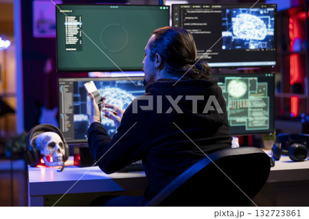 Hacker at desk coding on PC, using AI to evade security with stealth malware uploaded on SSD. Evil man using storage drive to hide malicious code from firewall detection systems 132723861