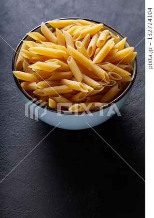 Dry Yellow Penne Pasta in Ceramic Bowl on Dark Background 132724104