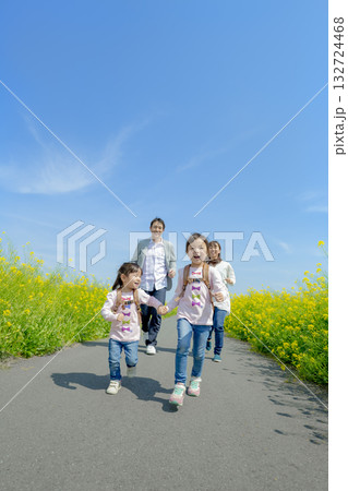 菜の花の咲く遊歩道を歩く4人家族 132724468