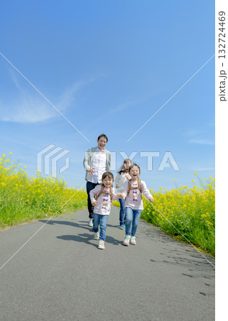 菜の花の咲く遊歩道を歩く4人家族 132724469