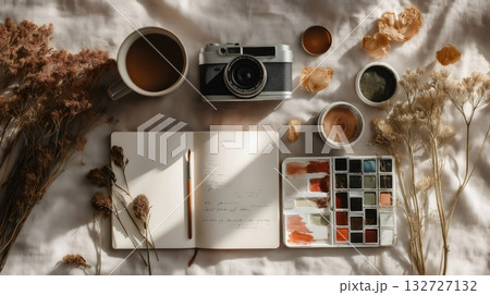 Watercolor set, vintage camera, coffee mug, dried flowers, and notebook with brush on beige linen sheet creating cozy artistic workplace atmosphere Watercolor set, vintage camera, coffee mug, dried flowers, and notebook with brush on beige linen sheet creating cozy artistic workplace atmosphere 132727132