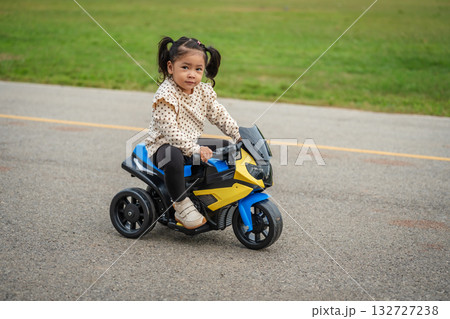 toddler girl riding an electric motorcycle toy in park 132727238
