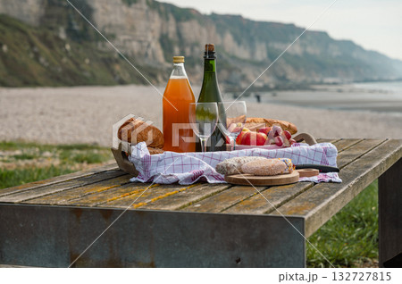 A cozy beach picnic in Normandy featuring French cidre, regional cheese, and fresh apples, set against a scenic coastal backdrop A cozy beach picnic in Normandy featuring French cidre, regional cheese, and fresh apples, set against a scenic coastal backdrop 132727815