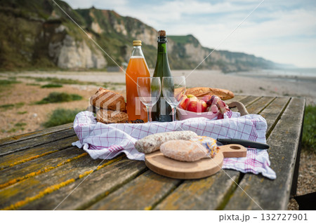 A cozy beach picnic in Normandy featuring French cidre, regional cheese, and fresh apples, set against a scenic coastal backdrop A cozy beach picnic in Normandy featuring French cidre, regional cheese, and fresh apples, set against a scenic coastal backdrop 132727901