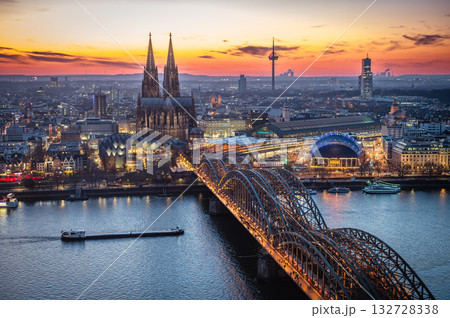 A breathtaking view of the Cologne skyline right after sunset featuring the iconic Cologne Cathedral and the city's famous bridge. The warm hues of the evening sky create a stunning scene in Germany. A breathtaking view of the Cologne skyline right after sunset featuring the iconic Cologne Cathedral and the city's famous bridge. The warm hues of the evening sky create a stunning scene in Germany. 132728338