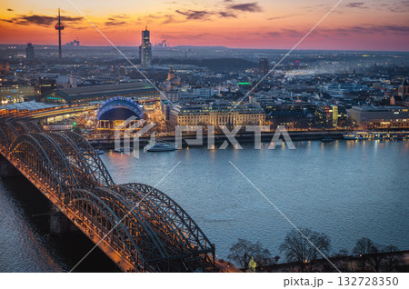 A breathtaking view of the Cologne skyline right after sunset featuring the iconic Cologne Cathedral and the city's famous bridge. The warm hues of the evening sky create a stunning scene in Germany. A breathtaking view of the Cologne skyline right after sunset featuring the iconic Cologne Cathedral and the city's famous bridge. The warm hues of the evening sky create a stunning scene in Germany. 132728350