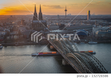 A breathtaking view of the Cologne skyline during sunset featuring the iconic Cologne Cathedral and the city's famous bridge. The warm hues of the evening sky create a stunning scene in Germany. A breathtaking view of the Cologne skyline during sunset featuring the iconic Cologne Cathedral and the city's famous bridge. The warm hues of the evening sky create a stunning scene in Germany. 132728386