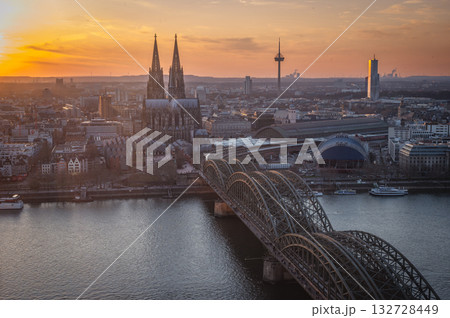 A breathtaking view of the Cologne skyline during sunset featuring the iconic Cologne Cathedral and the city's famous bridge. The warm hues of the evening sky create a stunning scene in Germany. A breathtaking view of the Cologne skyline during sunset featuring the iconic Cologne Cathedral and the city's famous bridge. The warm hues of the evening sky create a stunning scene in Germany. 132728449