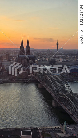 A breathtaking view of the Cologne skyline during sunset featuring the iconic Cologne Cathedral and the city's famous bridge. The warm hues of the evening sky create a stunning scene in Germany. A breathtaking view of the Cologne skyline during sunset featuring the iconic Cologne Cathedral and the city's famous bridge. The warm hues of the evening sky create a stunning scene in Germany. 132728494