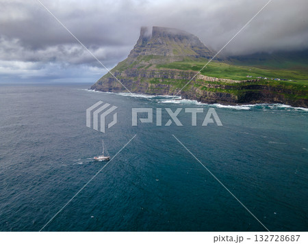 Dramatic Mulafossur waterfall plunging into the ocean with Gasadalur village and cliffs in the background. Dramatic Mulafossur waterfall plunging into the ocean with Gasadalur village and cliffs in the background. 132728687