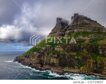Dramatic Mulafossur waterfall plunging into the ocean with Gasadalur village and cliffs in the background. 132728697