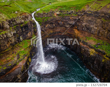 Dramatic Mulafossur waterfall plunging into the ocean with Gasadalur village and cliffs in the background. Dramatic Mulafossur waterfall plunging into the ocean with Gasadalur village and cliffs in the background. 132728704