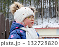 Outdoor winter portrait of little cute toddler girl in blue coat and white fashion hat. Healthy happy baby child playing in the park on cold day with snow and snowfall. Stylish clothes for kids 132728820