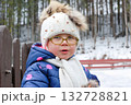 Outdoor winter portrait of little cute toddler girl in blue coat and white fashion hat. Healthy happy baby child playing in the park on cold day with snow and snowfall. Stylish clothes for kids 132728821