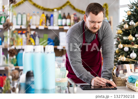Middle-aged man restocking using tablet in store with New Year decoration Middle-aged man restocking using tablet in store with New Year decoration 132730218