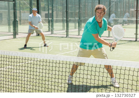 Padel game - man with partners plays on court 132730327