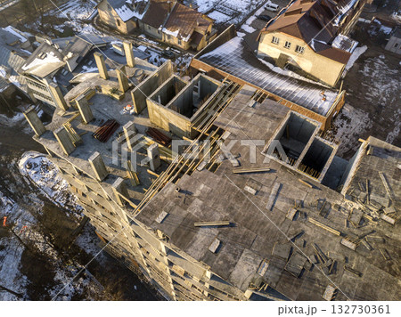 Aerial winter top view of modern developing city with tall apartment complex building under construction, parked cars, roofs and streets. Urban infrastructure, view from above. Aerial winter top view of modern developing city with tall apartment complex building under construction, parked cars, roofs and streets. Urban infrastructure, view from above. 132730361