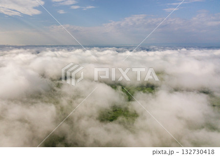 Aerial view of white clouds above a town or village with rows of buildings and curvy streets between green fields in summer. Countryside landscape from above. Aerial view of white clouds above a town or village with rows of buildings and curvy streets between green fields in summer. Countryside landscape from above. 132730418